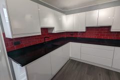 Wren handleless in white gloss, black quartz worktops, red metro tiles and a 4 in 1 tap
