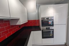 Wren handleless in white gloss, black quartz worktops, red metro tiles and a 4 in 1 tap